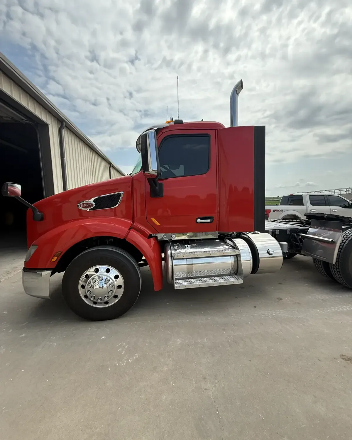 Red Peterbilt day-cab semi truck photographed against a dramatic sky